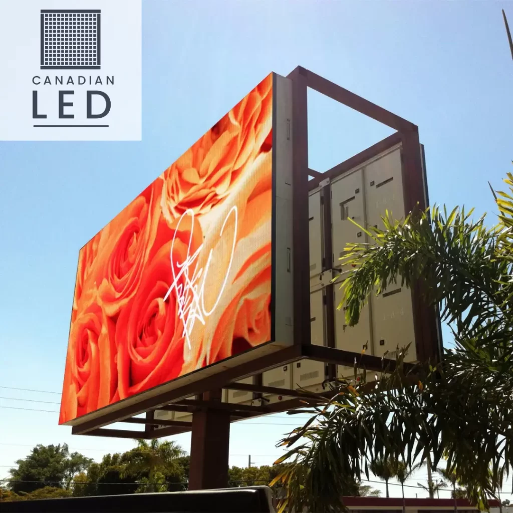 A large outdoor LED billboard displaying an image of orange roses under a bright blue sky.