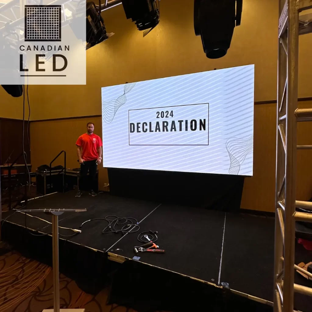A high-resolution LED screen on a stage displaying "2024 Declaration" with a technician in a red shirt standing beside it, set up for an indoor corporate event.