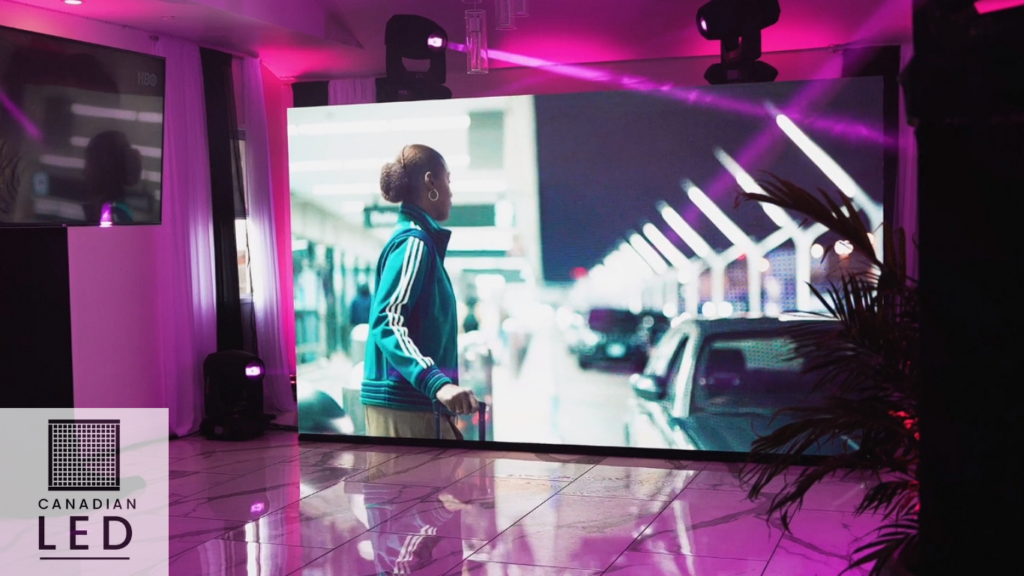 Indoor high-resolution LED display showing a woman at an airport scene, surrounded by purple event lighting.