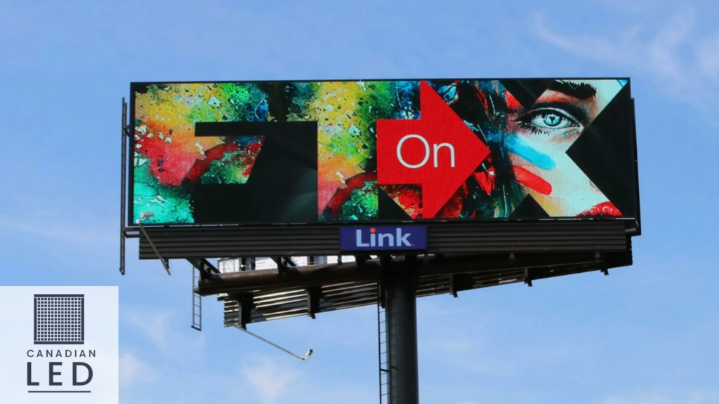 Large outdoor LED billboard displaying vibrant, colorful artwork with a red arrow and the word "On," under a clear blue sky.