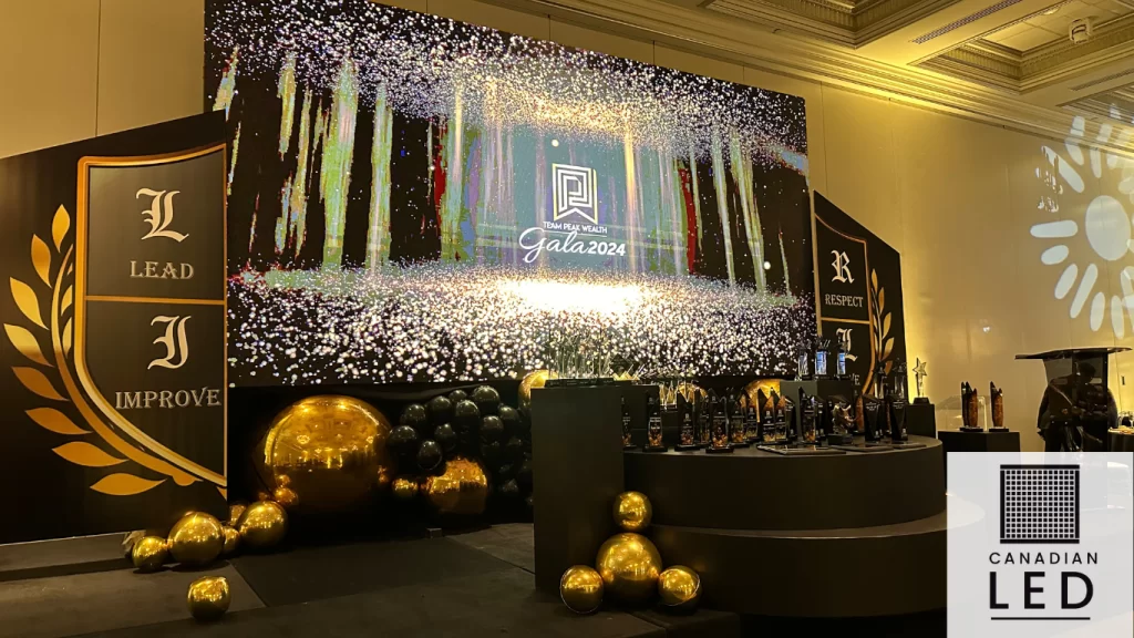 A grand LED display at the Team Peak Wealth Gala 2024, featuring a luxurious stage setup with gold and black decor, trophies, and elegant lighting effects.