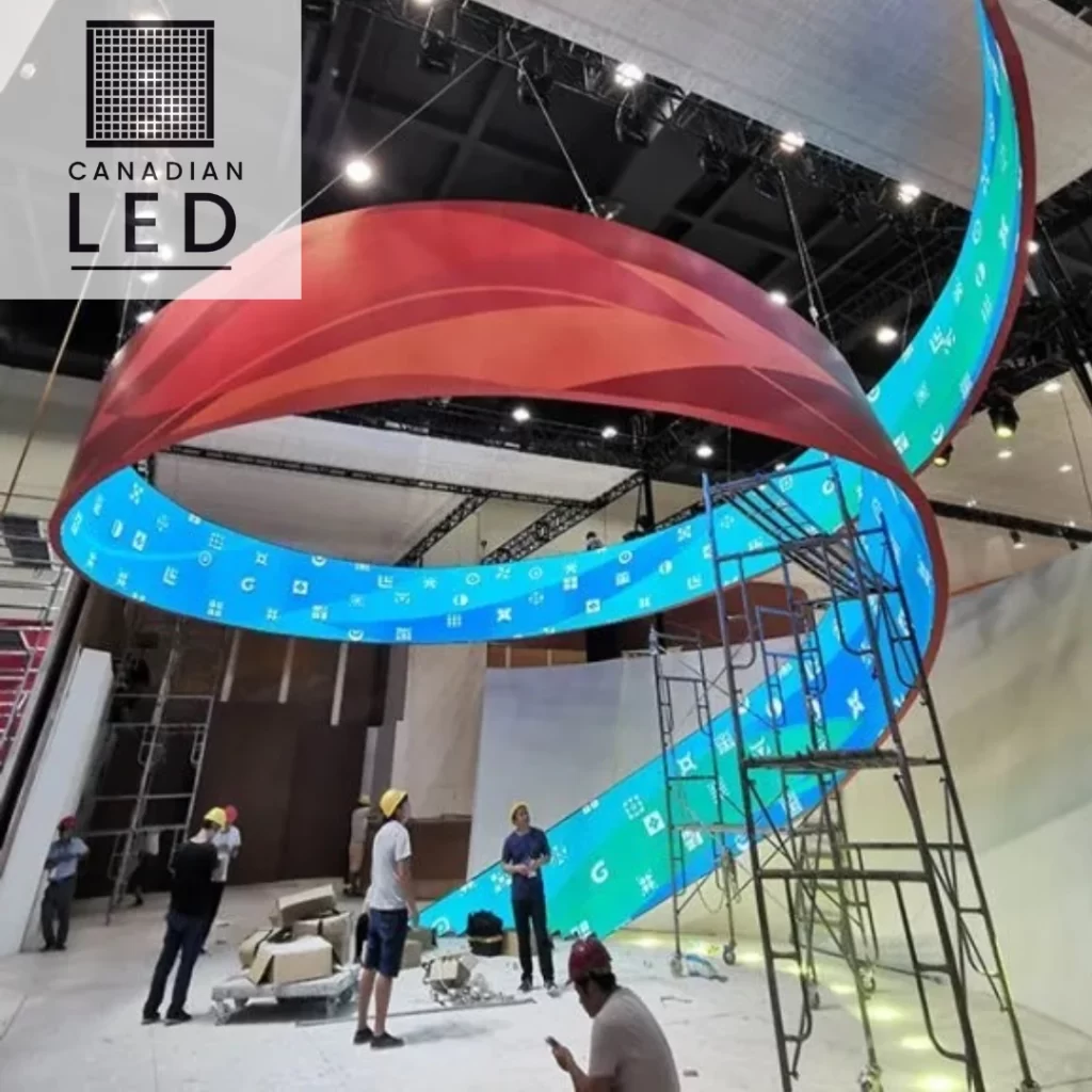 Large flexible LED screen installation in a spiral shape at an exhibition venue with workers setting up the display.