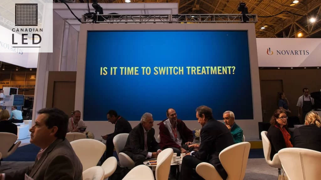 LED display at medical conference booth showing message “Is it time to switch treatment?” with attendees in discussion, Canadian LED branding visible.