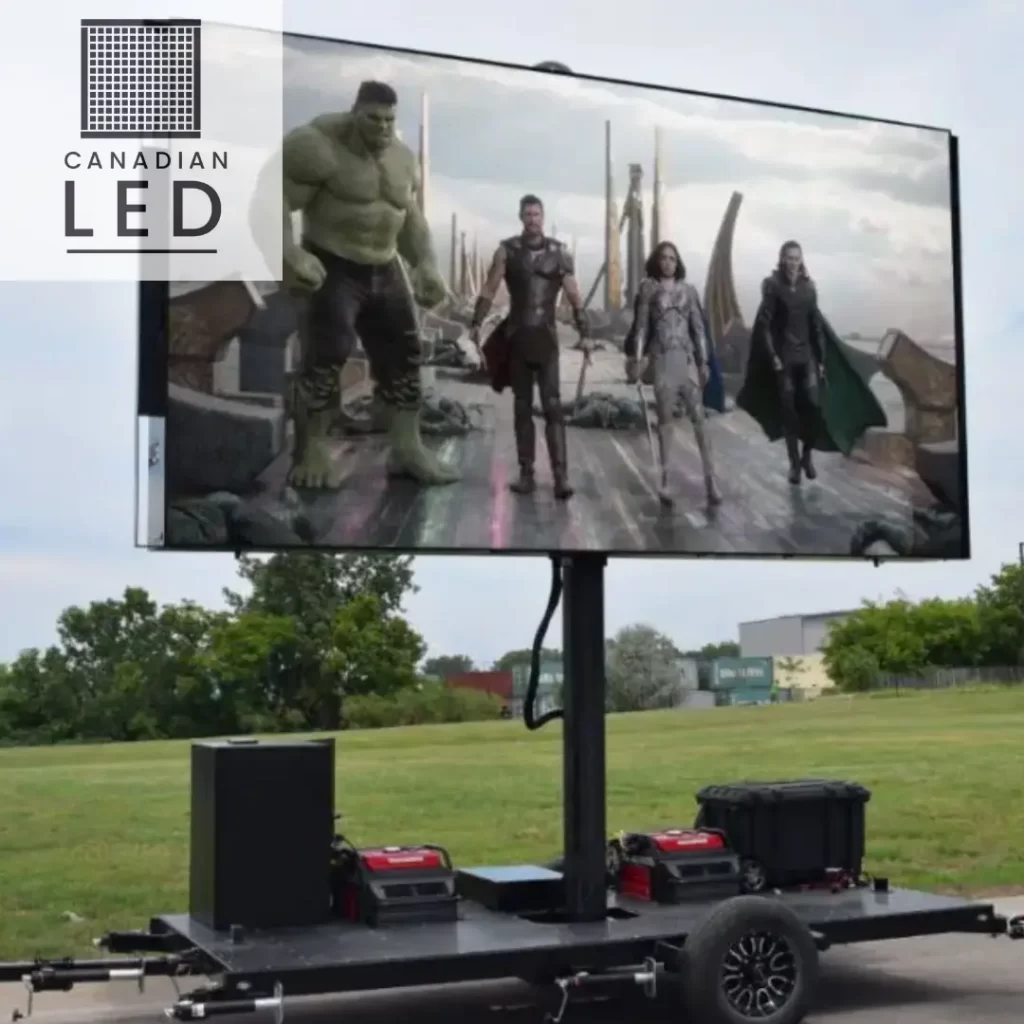 Outdoor mobile LED video wall on a trailer showing a scene from a superhero movie, set up on a grassy area.