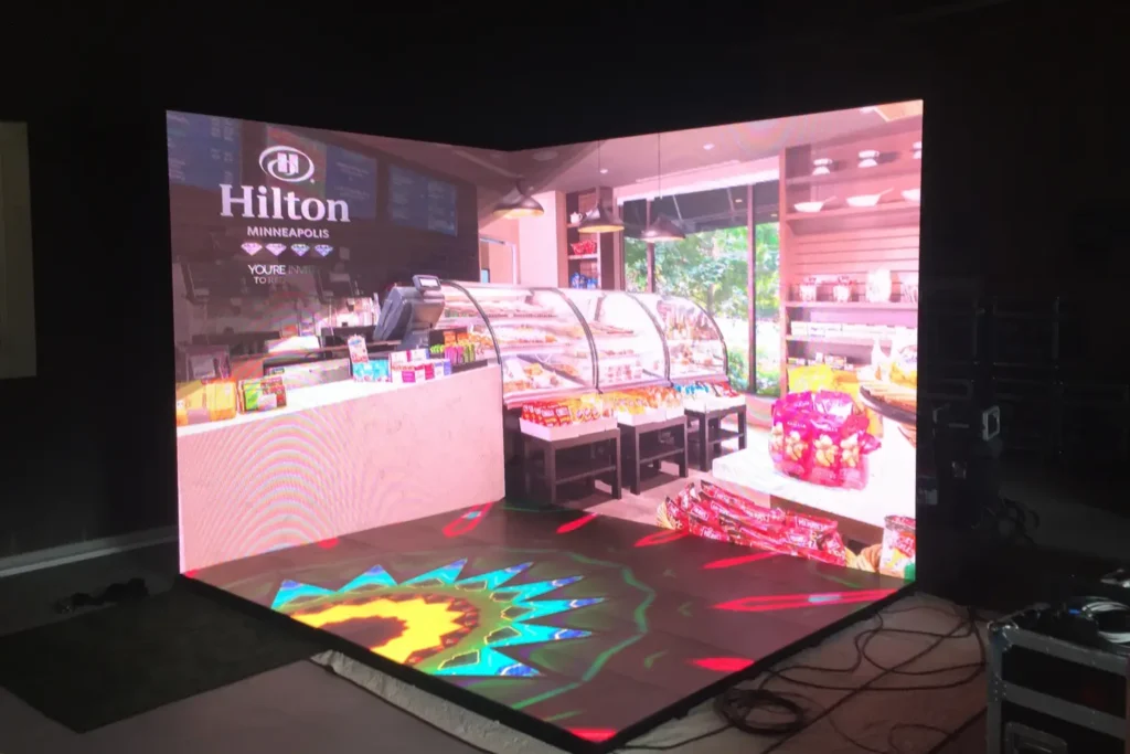 LED corner video wall display showing a Hilton Minneapolis café interior setup with product shelves and pastry cases.