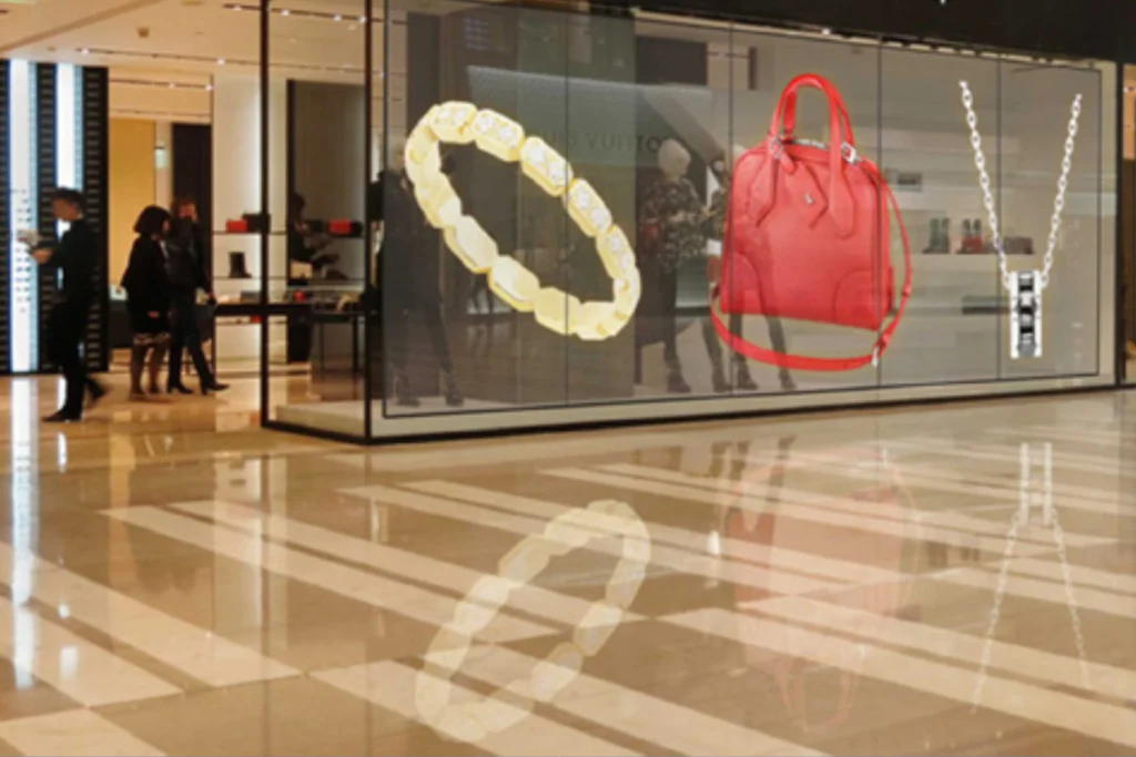 Transparent LED display showcasing luxury fashion items including a gold bracelet, red handbag, and silver necklace in a retail store.