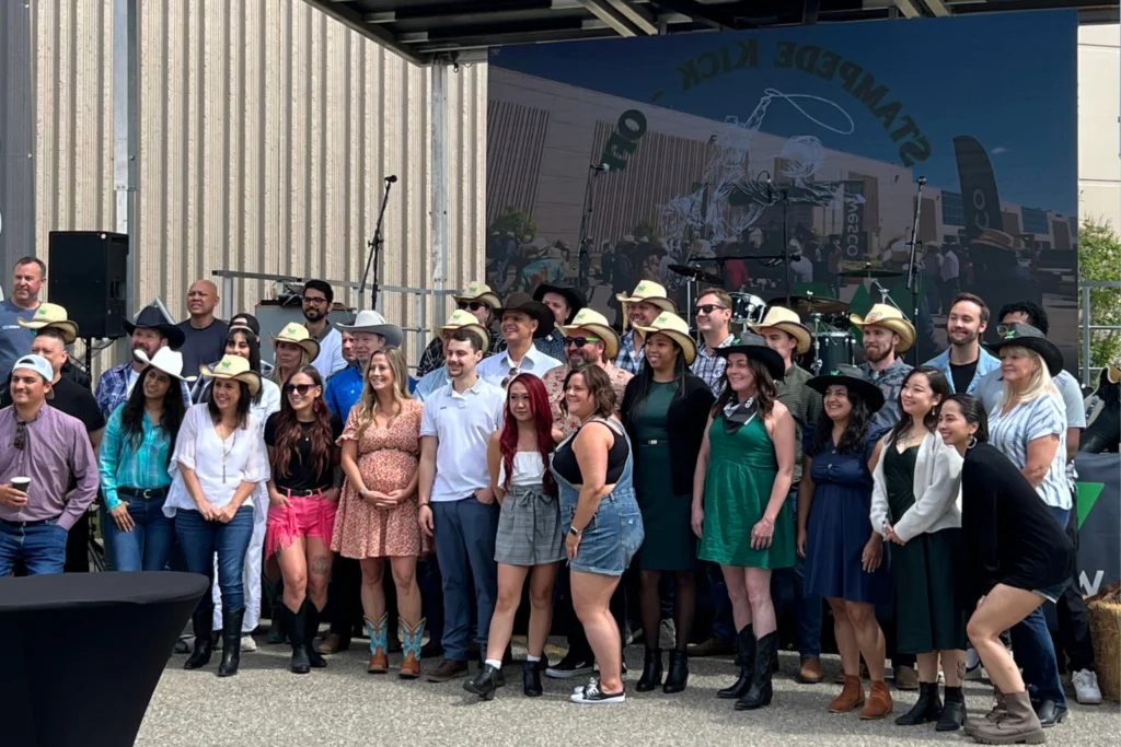 Coworkers at western-themed Stampede kickoff event posing in front of stage with hats and boots